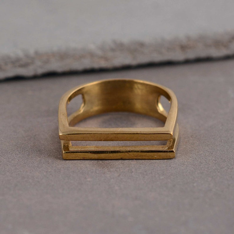 May include: A gold-toned ring with a double-bar design. The ring is made of metal and has a smooth, polished finish.