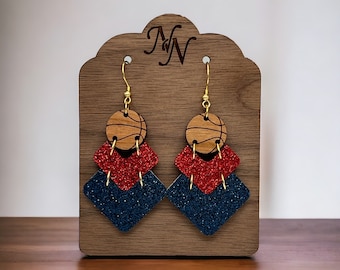 May include: A pair of dangle earrings with a basketball design. The earrings are made of wood and glitter. The basketball is brown and the glitter is red and blue.