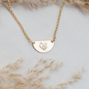 May include: A gold necklace with a delicate chain and a half-moon pendant featuring a floral design.