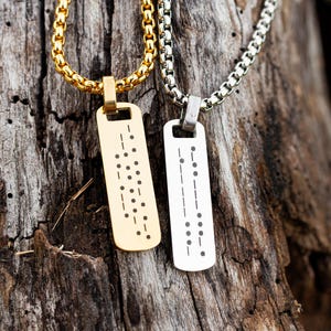 May include: Two rectangular pendant necklaces, one in gold tone and one in silver tone, each featuring a vertical arrangement of engraved dots and dashes in a Morse code pattern. Both pendants are suspended from matching box link chains.