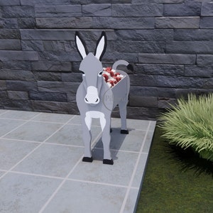 May include: A gray donkey-shaped planter with black ears and hooves. The planter's body is hollow, filled with red and white flowers. The donkey stands on a tiled surface in front of a dark gray stone wall. The planter is a unique garden decoration.