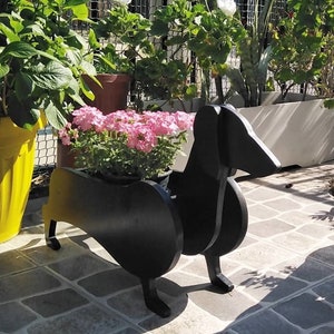 May include: Black wooden planter shaped like a dachshund dog with pink flowers in the planter.