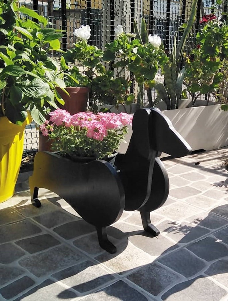 May include: Black wooden planter shaped like a dachshund dog with pink flowers in the planter.