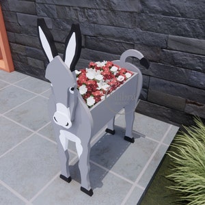 May include: A gray donkey-shaped planter filled with red and white flowers. The planter has black ears, hooves, and tail. The text "Libr&uacute; Creaciones" is visible on the side of the planter.
