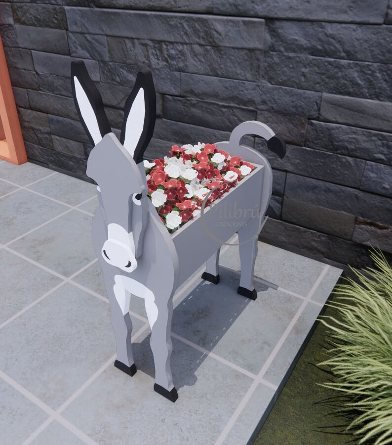 May include: A gray donkey-shaped planter filled with red and white flowers. The planter has black ears, hooves, and tail. The text "Libr&uacute; Creaciones" is visible on the side of the planter.