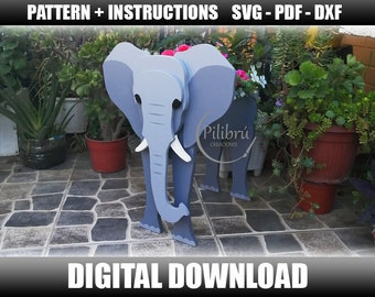 May include: A gray elephant planter with white tusks and black eyes. The planter is made of wood and has a cutout design. The planter is sitting on a patio with a stone floor. The planter is decorated with flowers. The text "Pilibrú Creaciones" is visible on the planter.
