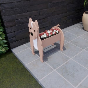 May include: A light brown planter shaped like a dog with white markings. The planter is filled with pink and white flowers. The planter is sitting on a gray tiled floor.