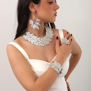 Op de afbeelding: Een zilveren blad ketting, armband en oorbellen set. De sieraden zijn gemaakt van met elkaar verbonden bladvormen.