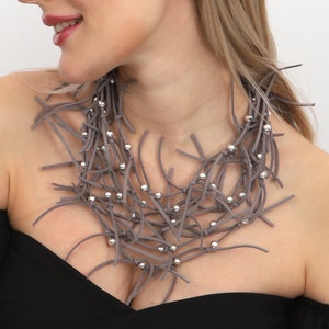 May include: A grey leather necklace with silver beads. The necklace is made of many strands of leather that are woven together. The beads are evenly spaced throughout the necklace.