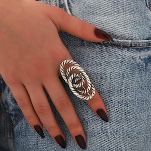 May include: A silver ring with a twisted rope design. The ring is oval shaped and has a textured finish.