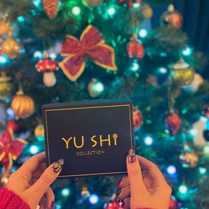 May include: A black box with gold lettering that reads "YU SHI COLLECTION" in front of a Christmas tree with colorful ornaments.