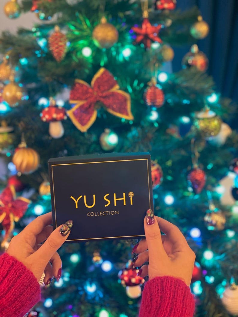 May include: A black box with gold lettering that reads "YU SHI COLLECTION" in front of a Christmas tree with colorful ornaments.