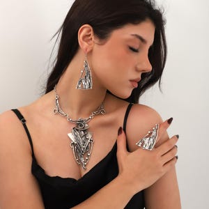 Peut inclure: Un ensemble de collier, boucles d'oreilles et bague en argent avec un design géométrique. Les bijoux présentent une forme triangulaire avec des détails complexes.