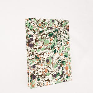 May include: A notebook with a marbled cover featuring a swirling pattern of green, brown, and orange. The cover has a white background with a variety of sized circles and swirls.
