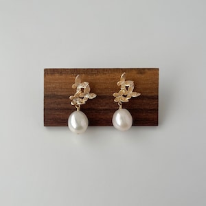 May include: Gold earrings with a delicate leaf design and a single white pearl dangling from each earring.
