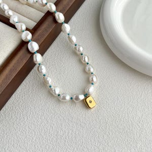 May include: A white pearl necklace with turquoise accents and a gold pendant with a small diamond. The necklace is on a wooden surface.