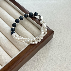 May include: A black and white pearl bracelet with a silver clasp. The bracelet is made of black beads and white pearls.