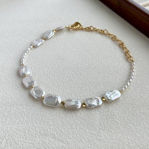 May include: A delicate gold chain necklace with a series of white baroque pearl beads. The pearls are irregularly shaped and have a subtle shimmer.