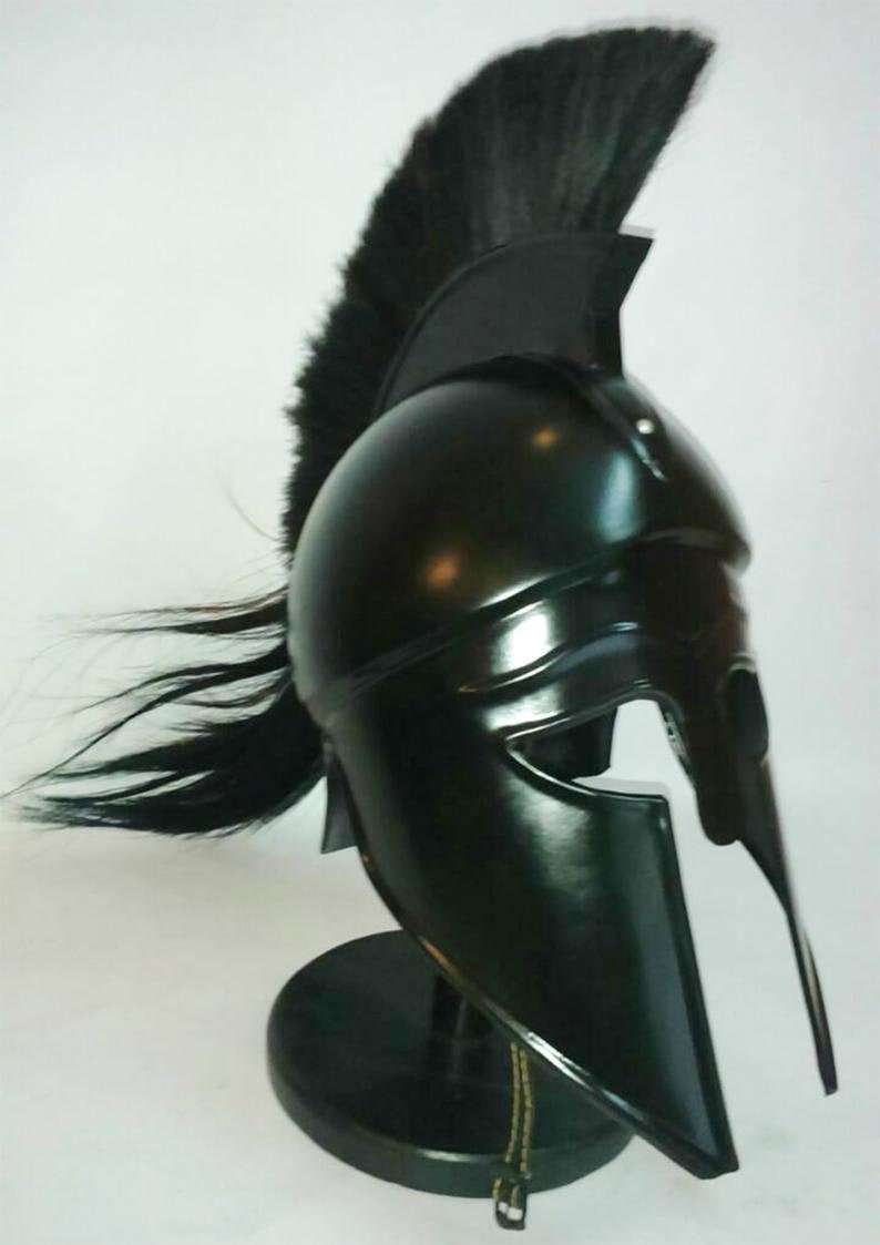 K&ouml;nnte beinhalten: Ein schwarzer spartanischer Helm mit einer schwarzen Rosshaar-Feder auf einem schwarzen St&auml;nder. Der Helm hat einen markanten Wangenschutz und eine erh&ouml;hte Spitze.