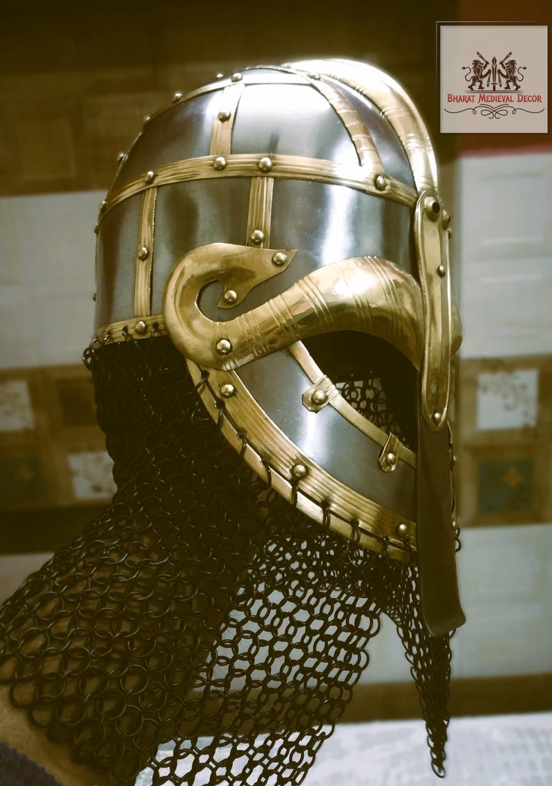 May include: A medieval-style helmet with a polished silver finish and ornate gold-colored accents. The helmet features riveted gold bands, decorative cheek guards, and a chainmail neck guard. The design is reminiscent of historical armor.