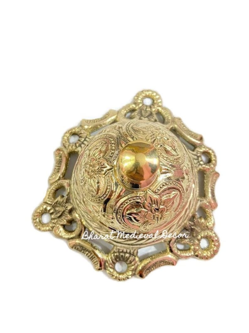 May include: A gold-toned metal bell with an ornate design. The bell has a round top and a decorative base. The bell is a traditional design.
