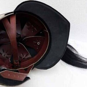 Puede incluir: Un casco medieval con una visera de cuero negro y una larga pluma de crin de caballo negra. El casco est&aacute; hecho de metal y tiene un interior de cuero marr&oacute;n.