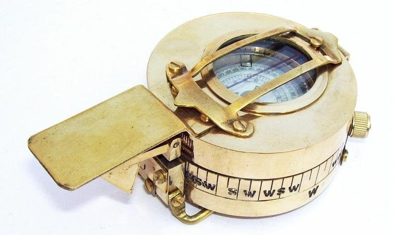 May include: A brass compass with a folding lid and a compass dial with a needle. The compass has a scale on the side with markings for directions.