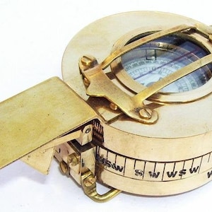 May include: A brass compass with a folding lid and a compass dial with a needle. The compass has a scale on the side with markings for directions.