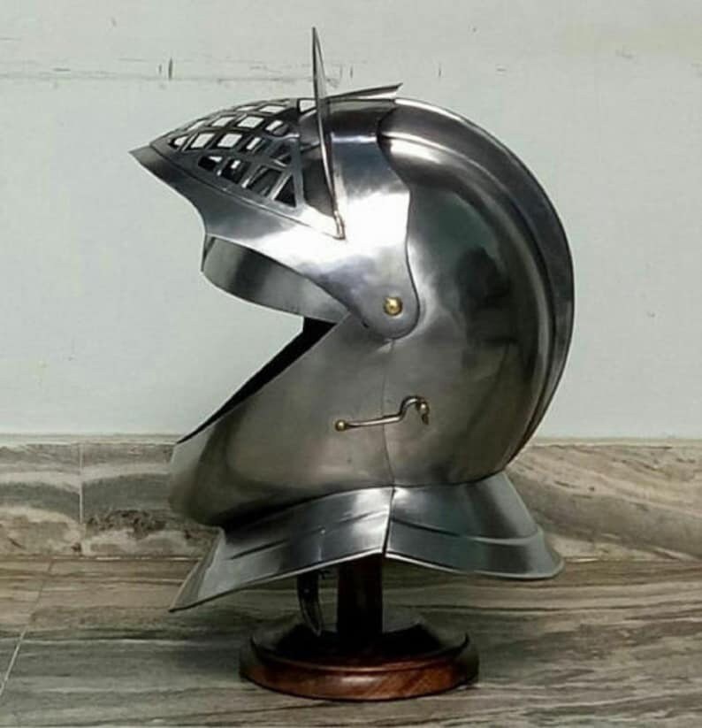 May include: A silver helmet with a visor and a decorative grill on the top. The helmet is on a wooden stand.