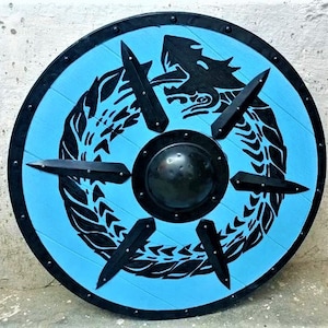 May include: A round wooden shield with a blue background and a black dragon design. The shield has a metal center boss and is decorated with metal rivets around the edge.