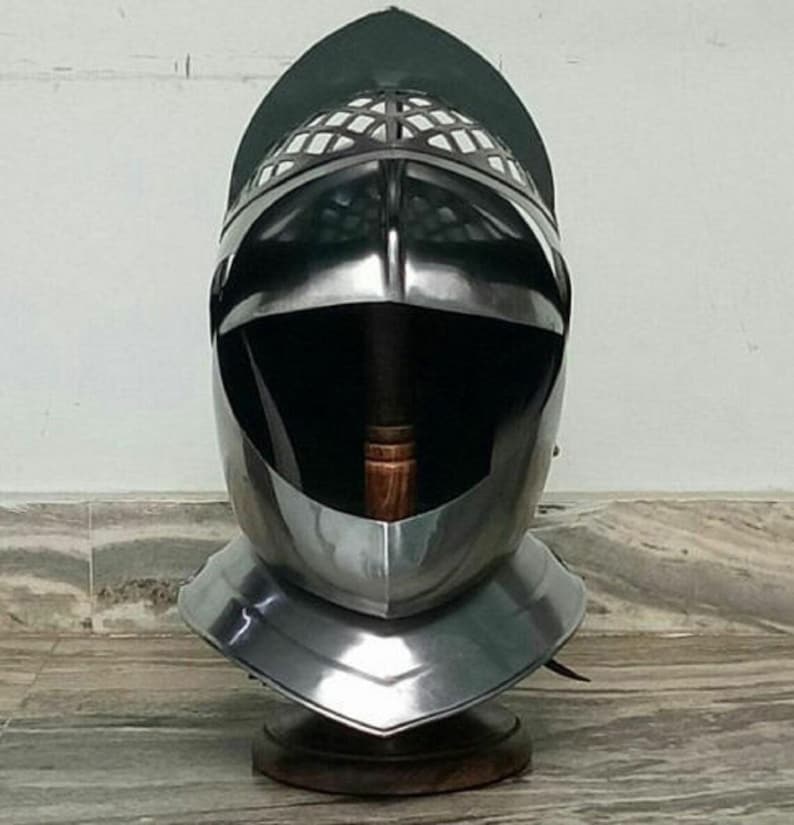 May include: A silver helmet with a visor and a decorative metal grille. The helmet is on a wooden stand.