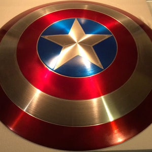 May include: A red, white, and blue Captain America shield with a silver star in the center. The shield is made of metal and has a shiny finish.