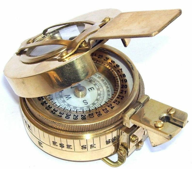 May include: A brass compass with a hinged lid and a compass face with numbers 1 through 36. The compass has a white face with black markings and a black needle. The compass is on a white background.
