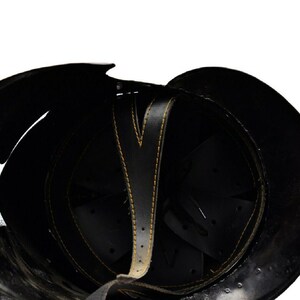 Puede incluir: El interior de un casco negro con una correa de cuero negro y costuras amarillas. El casco tiene una serie de secciones acolchadas negras en el interior.