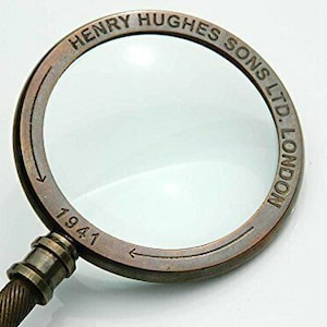 May include: Antique brass magnifying glass with a round lens and a handle. The glass has the inscription "HENRY HUGHES SONS LTD. LONDON 1941" around the rim.