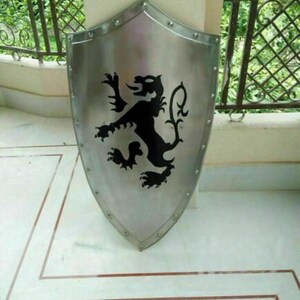Puede incluir: Un escudo plateado con un dise&ntilde;o de le&oacute;n negro. El escudo est&aacute; hecho de metal y tiene una parte superior redondeada y una parte inferior puntiaguda.