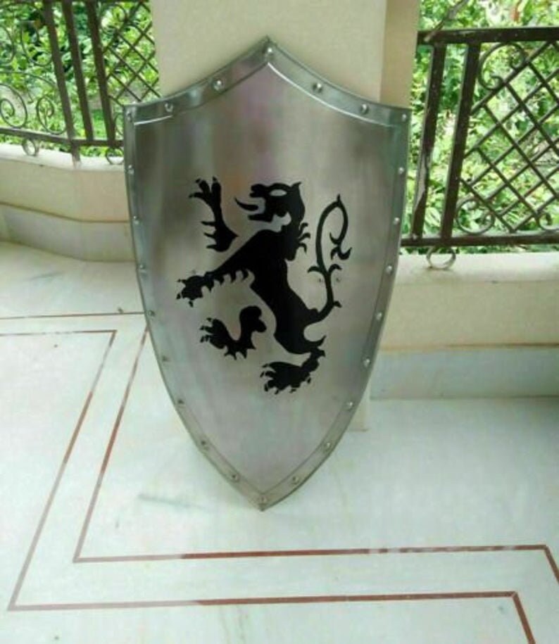 Puede incluir: Un escudo plateado con un dise&ntilde;o de le&oacute;n negro. El escudo est&aacute; hecho de metal y tiene una parte superior redondeada y una parte inferior puntiaguda.