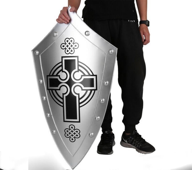 Puede incluir: Un escudo plateado con un dise&ntilde;o de cruz celta negra. El escudo tiene una parte superior redondeada y una parte inferior puntiaguda. Est&aacute; decorado con peque&ntilde;os remaches met&aacute;licos alrededor del borde.