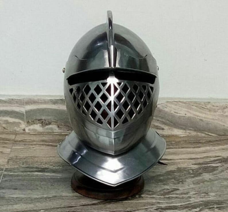 May include: A silver knight's helmet with a visor featuring a diamond-shaped grill pattern. The helmet has a pointed crest and a decorative chin guard.