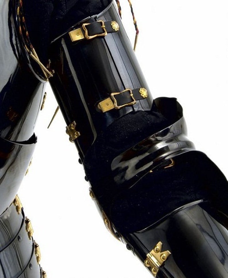 Op de afbeelding: Close-up van een zwart metalen armstuk van een harnas met gouden accenten en leren banden. Het harnas is scharnierend en heeft een decoratief ontwerp.