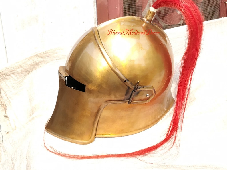 May include: A polished brass helmet with a red plume. The helmet has a rounded top, a visor, and a chin guard. The plume is attached to the top of the helmet and hangs down the back. The helmet is likely a historical or costume piece.