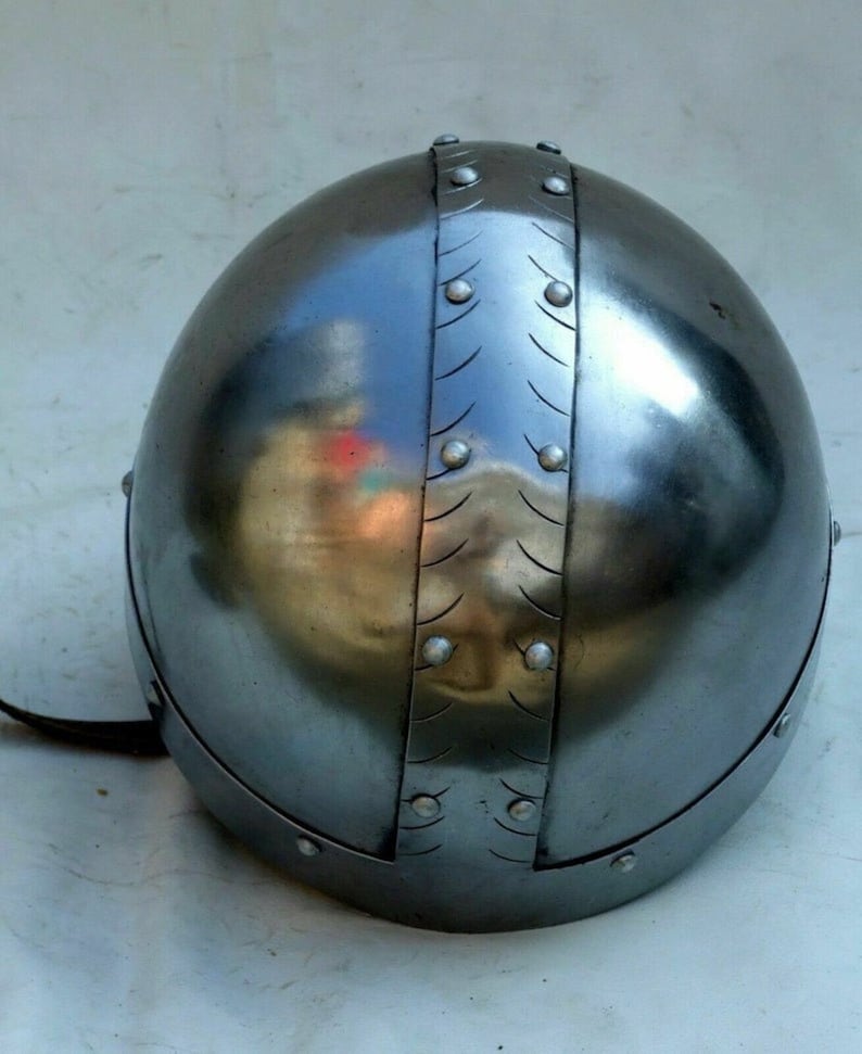 Pu&ograve; includere: Un elmo d'argento con una cupola arrotondata e una fascia decorativa di rivetti metallici. L'elmo ha un cinturino in pelle attaccato al lato.