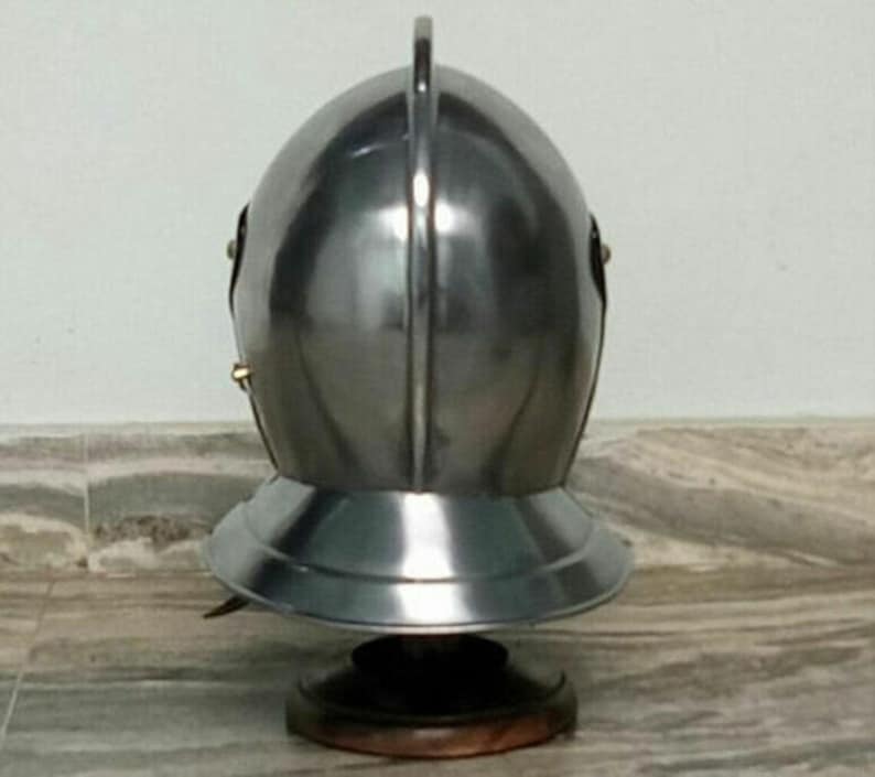 May include: A silver helmet with a pointed top and a brim. The helmet is on a wooden stand.