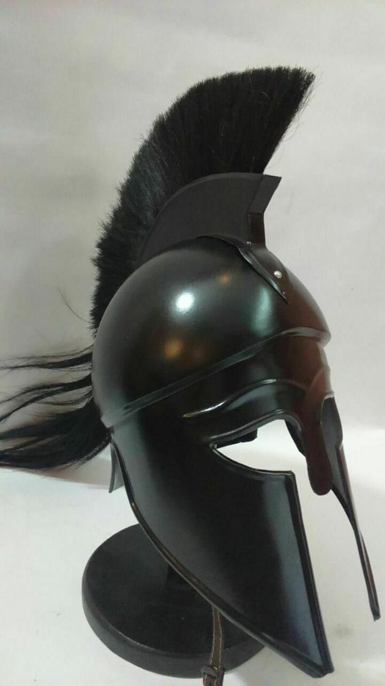 K&ouml;nnte beinhalten: Ein schwarzer spartanischer Helm mit einer schwarzen Rosshaar-Feder. Der Helm steht auf einem schwarzen St&auml;nder.