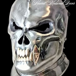 Puede incluir: Un casco de calavera de plata con una expresi&oacute;n amenazante. El casco tiene una parte superior puntiaguda y una cara de calavera detallada con dientes afilados. El casco est&aacute; hecho de metal y tiene una superficie texturizada.