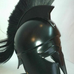 K&ouml;nnte beinhalten: Ein schwarzer spartanischer Helm mit einer schwarzen Rosshaar-Feder. Der Helm steht auf einem schwarzen St&auml;nder.