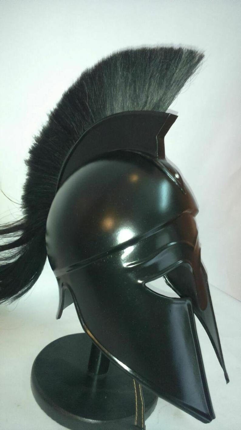 K&ouml;nnte beinhalten: Ein schwarzer spartanischer Helm mit einer schwarzen Rosshaar-Feder. Der Helm steht auf einem schwarzen St&auml;nder.