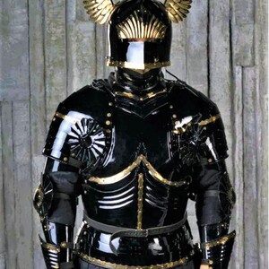 May include: A black and gold knight's armor with a helmet featuring golden wings. The armor is detailed with gold accents and rivets.
