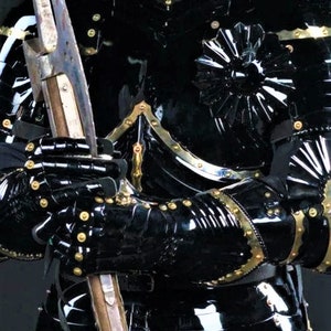 May include: Black and gold medieval armor with a decorative design on the chest and shoulder. The armor is made of metal and has a glossy finish.