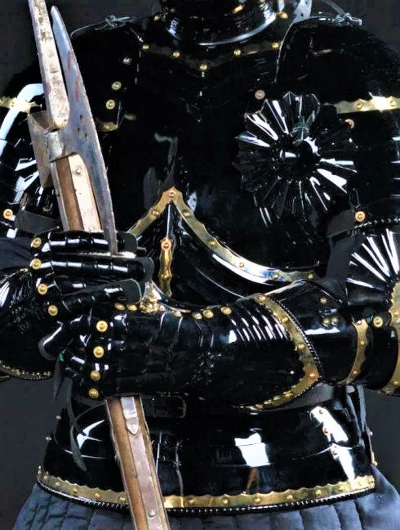 May include: Black and gold medieval armor with a decorative design on the chest and shoulder. The armor is made of metal and has a glossy finish.